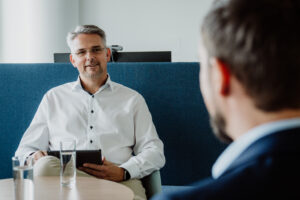 York Ambros frontal im weißen Hemd, wie er einer anderen Person freundlich etwas erklärt