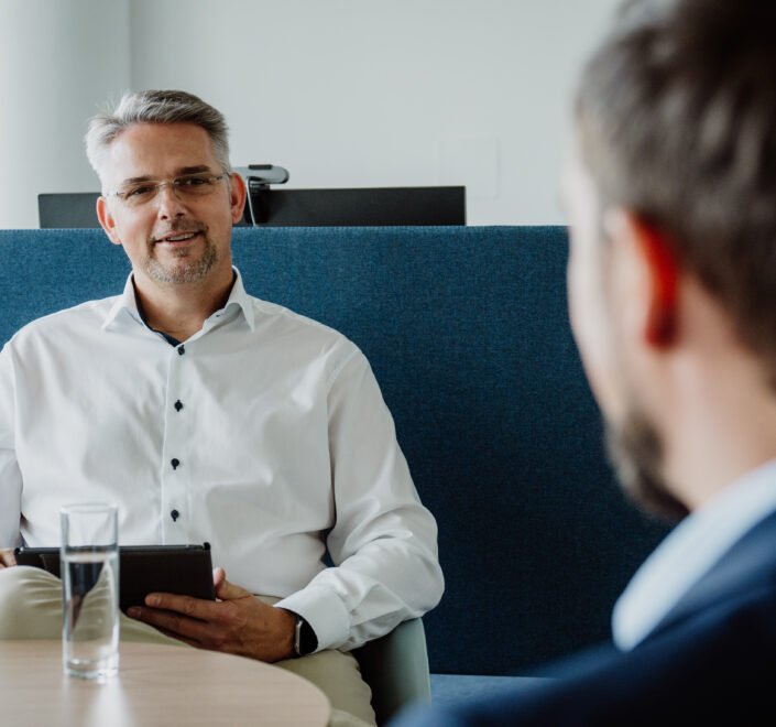 York Ambros frontal im weißen Hemd, wie er einer anderen Person freundlich etwas erklärt
